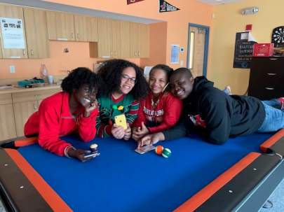 4 smiling teenagers leaning on a pool table