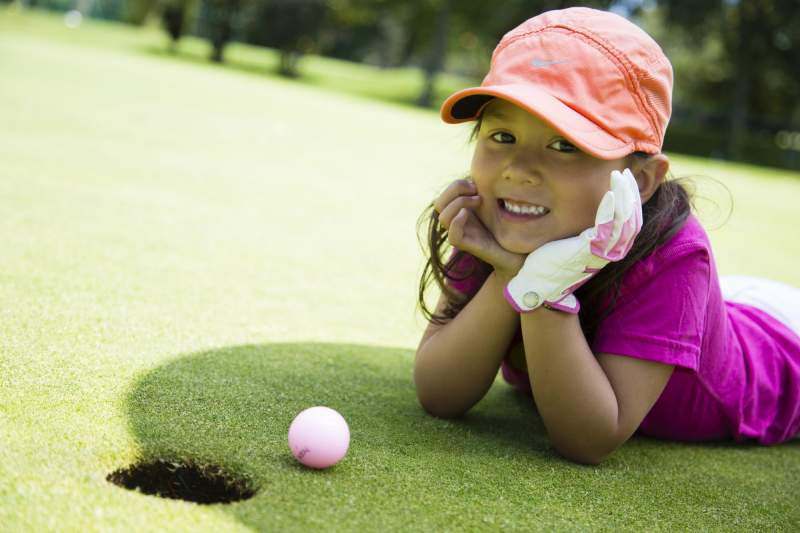 Young girl wearing pink smiling in front of golf ball