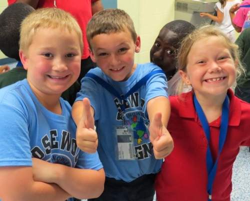 Three children smiling, one with thumbs up